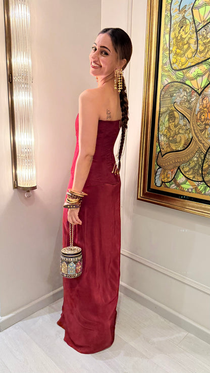 A woman models a strapless burgundy velvet gown with a sweetheart neckline and a flowing skirt, standing in a warmly lit interior next to a wall sconce and framed artwork.

Ridhi Khosla Jaan in baavli
Sourced by Design Aura