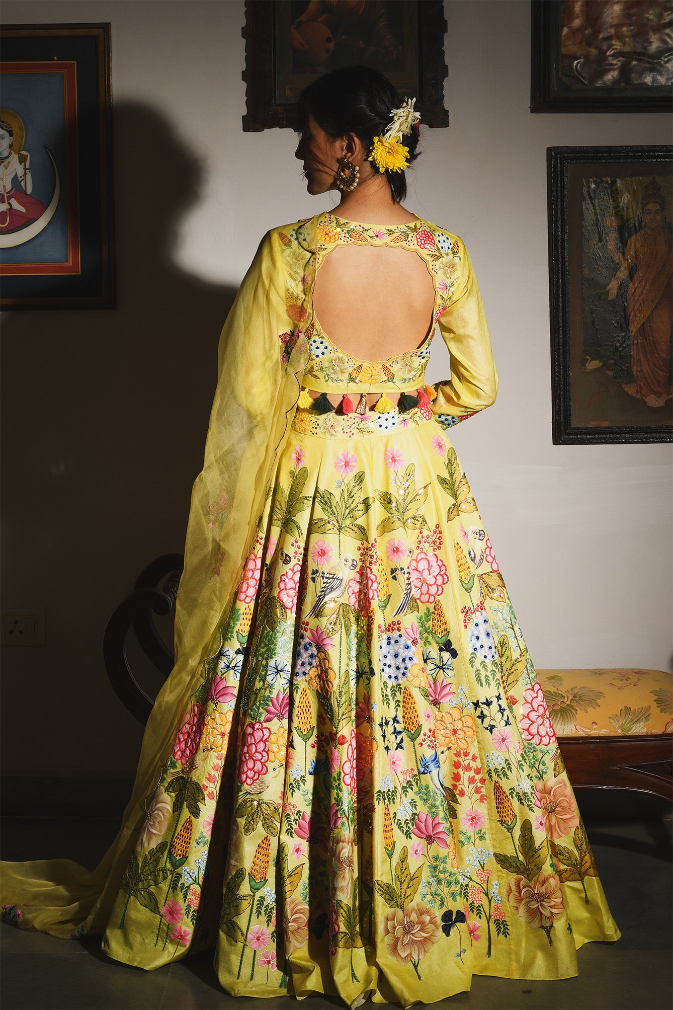 Woman wearing a vibrant yellow floral dress in an indoor setting with framed pictures on the wall.

