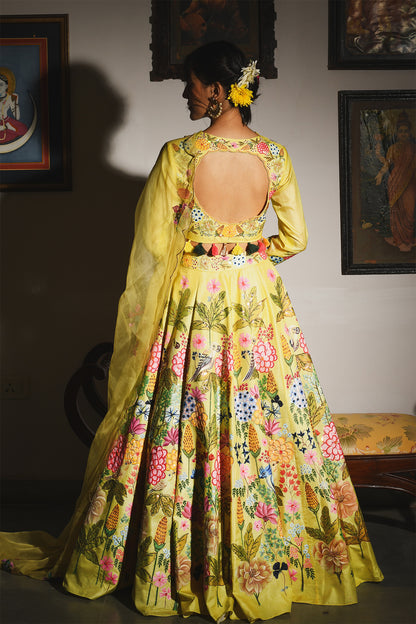 Woman wearing a vibrant yellow floral dress in an indoor setting with framed pictures on the wall.

