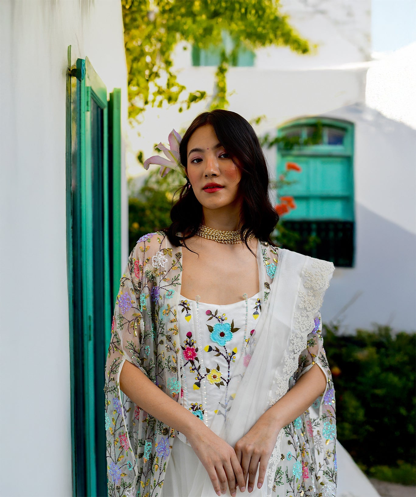 Woman in a floral dress and cardigan standing in front of a white building with green shutters.

designer label
expensive saree
